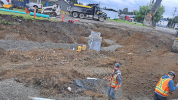 Deux hommes de la construction en dossard orange, sur le chantier des travaux de la rue Notre-Dame à Kedgwick, lors d'une journée d'été nuageuse.