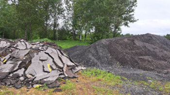 Un tas d'asphalte déchiqueté à gauche ainsi qu'un tas d'asphalte recyclé à droite, à l'extérieur lors d'une journée d'été nuageuse.