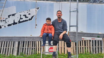 Un papa et son fils à l'extérieur, assis côte-à-côte sur une poutre de bois pour une photo.