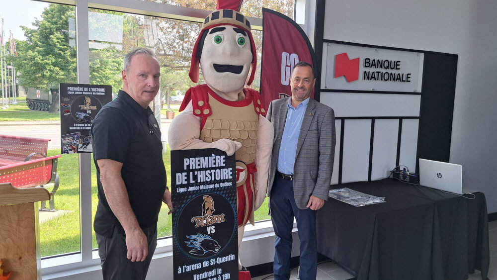 Deux hommes aux côtés de la mascotte du Titan d'Acadie Bathurst au Palais Centre-Ville de Saint-Quentin.