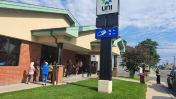 Une file d'attente d'une quinzaine de personnes devant l'UNI Coopération financière de Saint-Quentin, lors d'une journée ensoleillée.