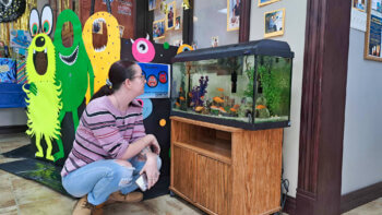 Une femme accroupie et regarde de près un aquarium dans une bibliothèque.