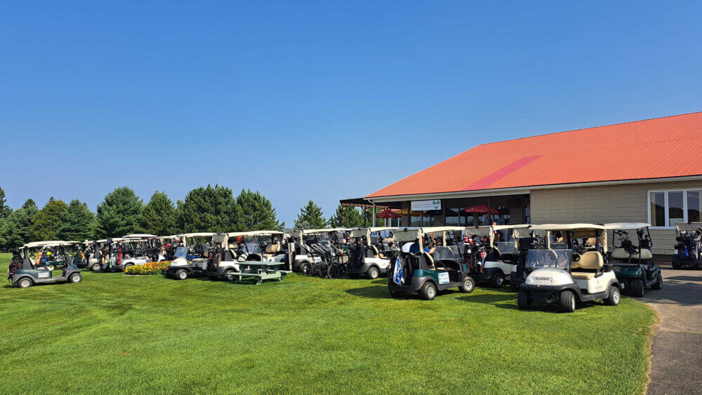 Plusieurs voiturettes de golfs devant un bâtiment au toit orange, lors d'une journée chaude et ensoleillée.