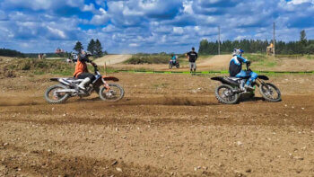 Deux pilotes de motocross en action sur la piste prenant un virage à gauche, lors d'une journée ensoleillée.