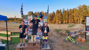 3 jeunes motocyclistes sur un podium après une compétition de motocross, lors d'une journée ensoleillée.