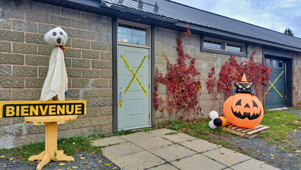 Un hangar construit en pierres avec un toi en tôle, des décorations d'halloween sont installées devant la porte d'entrée, un fantôme à gauche et une citrouille à droite.
