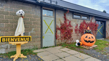 Un hangar construit en pierres avec un toi en tôle, des décorations d'halloween sont installées devant la porte d'entrée, un fantôme à gauche et une citrouille à droite.