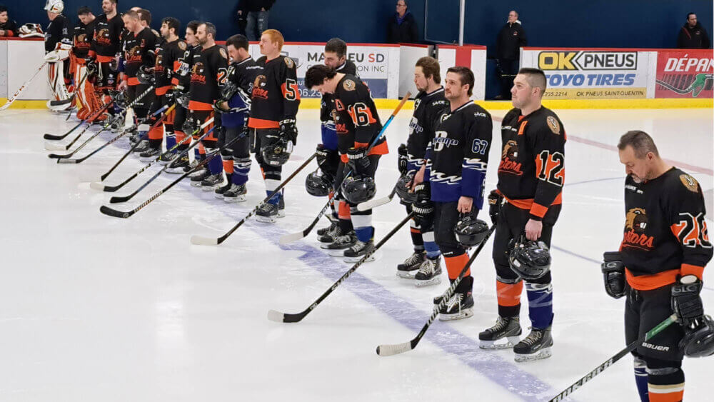 Des joueurs de hockey en uniforme foncé sont alignés sur la ligne bleue d'une patinoire à l'intérieur d'un aréna.