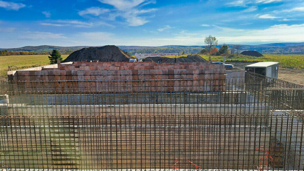 Un réservoir d'eau potable en construction, on peut voir des grilles de fers et des murs de ciment, pendant une journée ensoleillée.