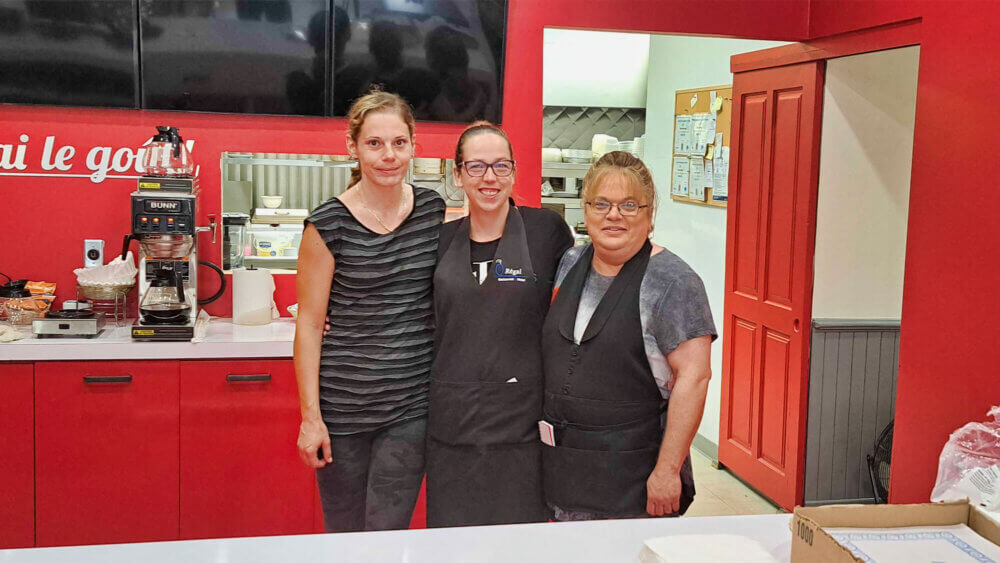 Trois serveuses d'un restaurant derrière un comptoir se tiennent côte à côté pour une photo.