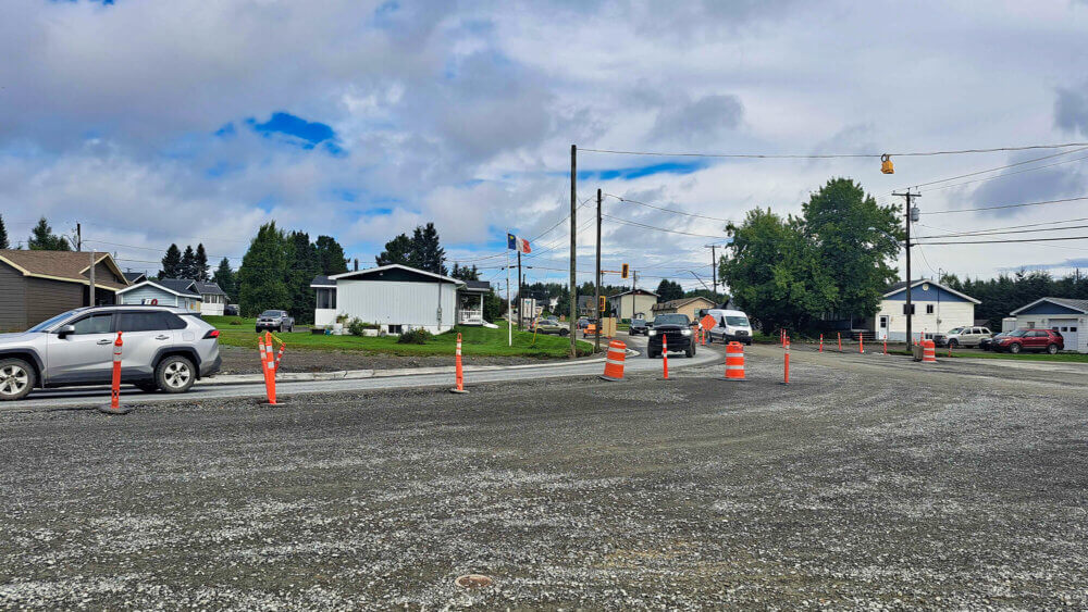 Chantier de construction routière sur la rue Notre-Dame à Kedgwick, les véhicules circulent sur une voie à travers les cônes orange lors d'une journée nuageuse.