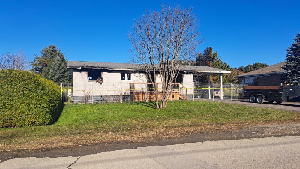 Une maison beige endommagée par les flammes derrière une arbre sans feuille lors d'une journée de novembre ensoleillée