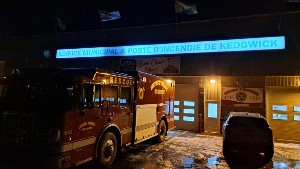 : Camion de pompier rouge devant une caserne lors d'une nuit très sombre où il n'y pas d'électricité.
