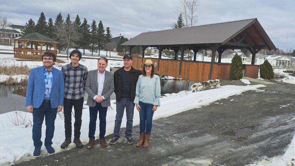 Quatre hommes et une femme se tiennent debout à l'extérieur devant le pont Rodolphe Lavoie à Kedgwick, lors d'une douce journée d'hiver