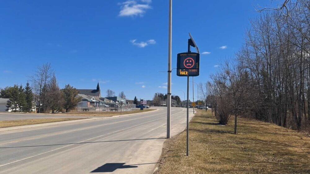 Panneau d'affichage de vitesse à l'entrée du village de Kedgwick, qui affiche un émoticône triste. Le ciel et dégagé en cette journée de printemps.