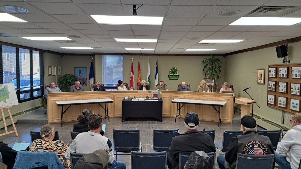 Des citoyens assistent à une réunion publique mensuelle du conseil de ville de Saint-Quentin. Les 6 conseillers et la mairesse sont assis devant eux.