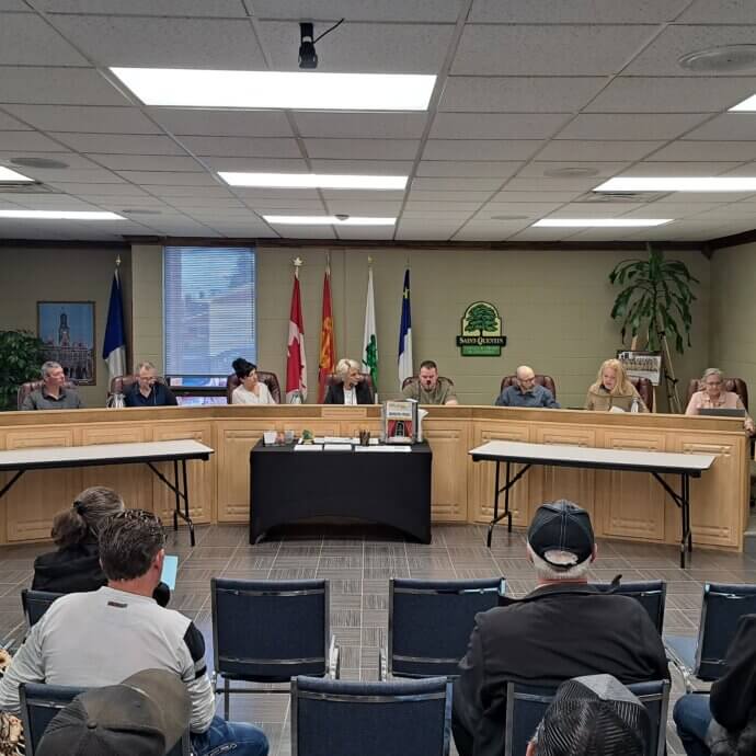 Des citoyens assistent à une réunion publique mensuelle du conseil de ville de Saint-Quentin. Les 6 conseillers et la mairesse sont assis devant eux.