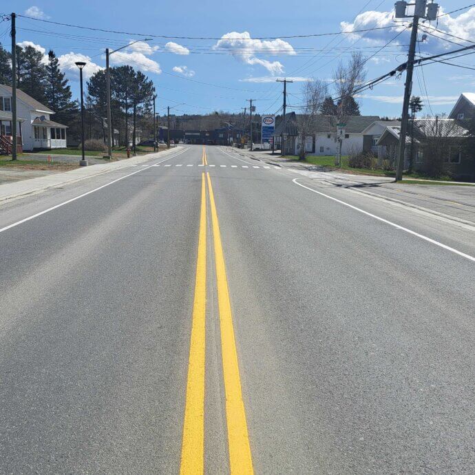 La rue Notre-Dame à Kedgwick. Photo prise en pleine centre de la ligne double jaune sur une rue asphaltée neuve, lors d'une journée de mai ensoleillée.