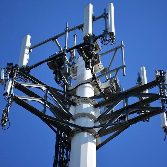 Vue sur le haut d'une tour de projection d'ondes cellulaires. Le ciel est complètement dégagé.